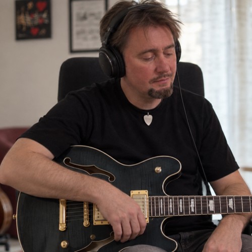 Max Gotta nel suo studio con le cuffie, mentre ascolta con una chitarra semiacustica in grembo