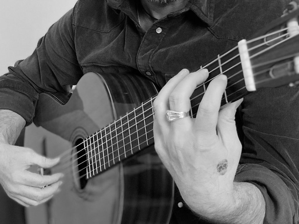 Le mani di Max Gotta che suonano con le dita su una chitarra acustica, in primo piano